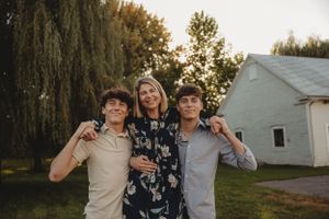 Three people pose together outdoors at sunset near a white building.