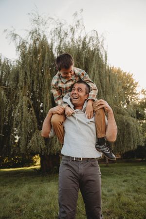 A heartwarming piggyback ride scene with laughter and joy under willow trees.