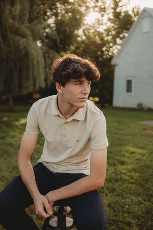 Casual outdoor portrait of young person in beige polo shirt sitting near white building at sunset.