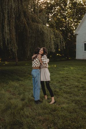 Two people sharing an embrace on grass near a white house at sunset.