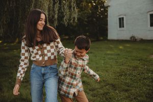 A pair shares a playful moment walking together in a backyard with a white house and willow tree.