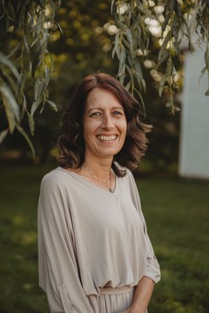 A relaxed portrait of someone in casual attire standing beneath willow branches.