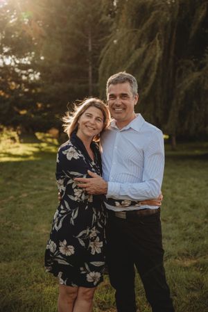 A couple embraces in warm sunset light beneath a weeping willow tree.
