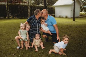 Family group poses together on grass in front of white building during outdoor photo session.