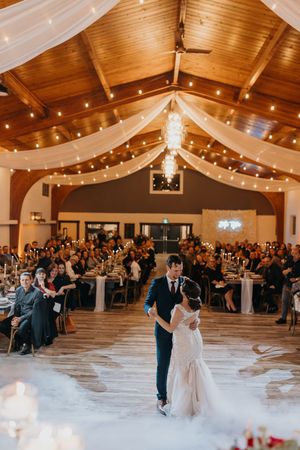 bride and groom dancing their first dance at urban field house under string lights with loved ones watching