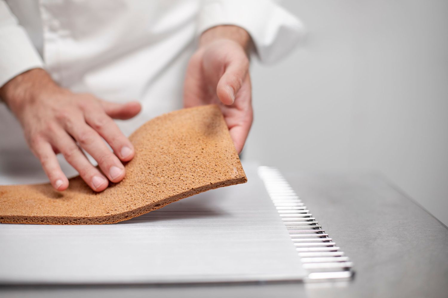 Hands working with cork material on a light grey surface showing craftsmanship detail.