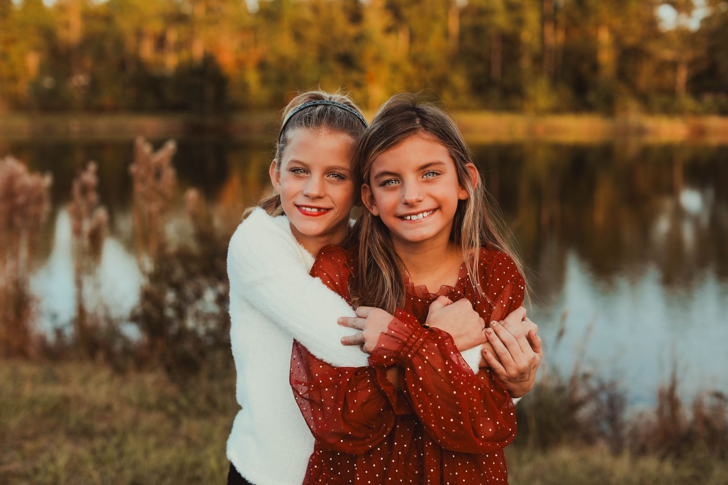 Two people hugging and smiling by autumn lake with golden trees in background.