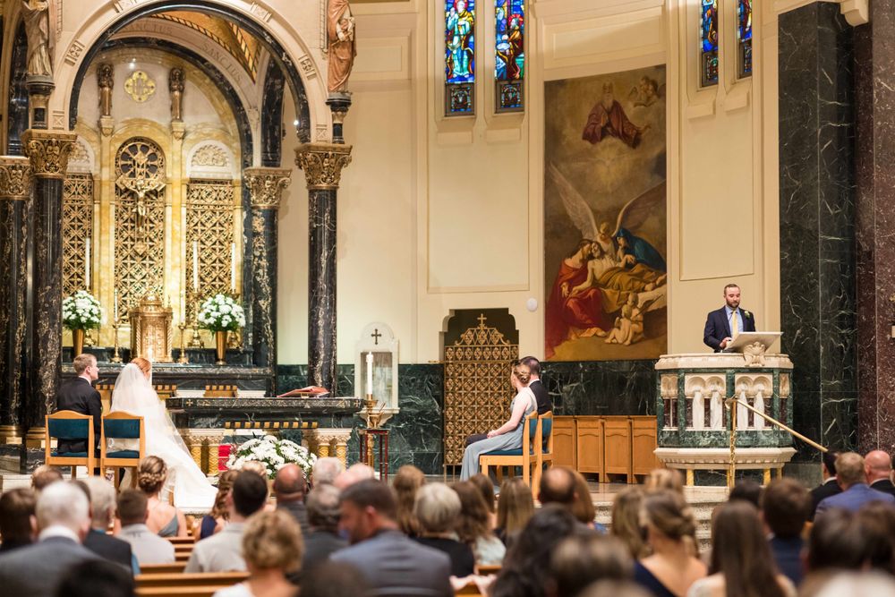 Church interior with ornate arches, stained glass windows and religious artwork during ceremony.