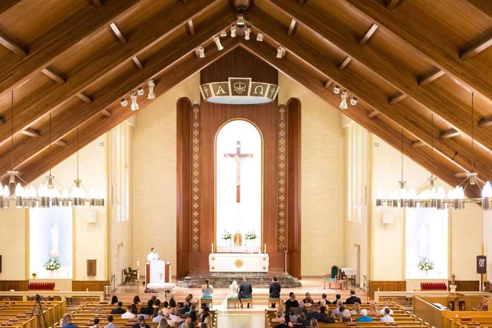 Modern church interior with wooden beams and large cross at altar during wedding ceremony.