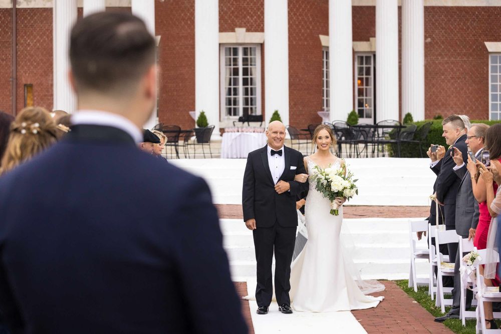 Traditional wedding ceremony processional at elegant brick building with white columns.