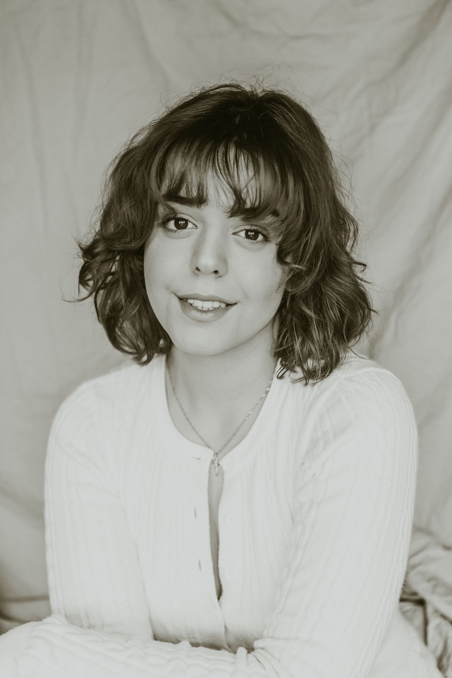 Black and white portrait of person in white sweater against plain backdrop.