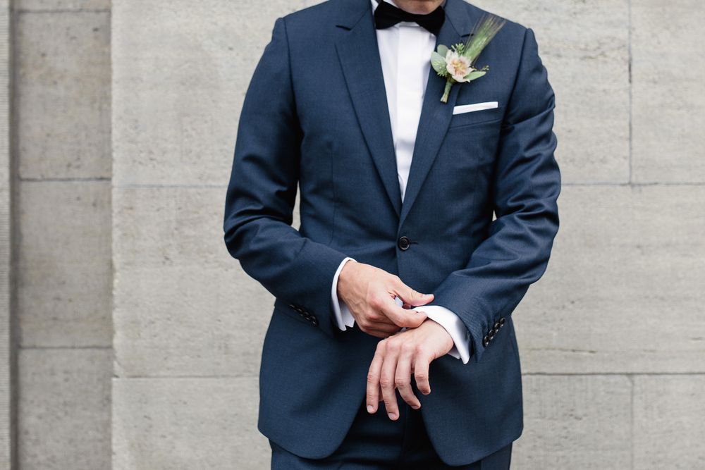 Vertical close-up portrait of a groom in a dark suit, focusing on the floral boutonniere and formal attire.
