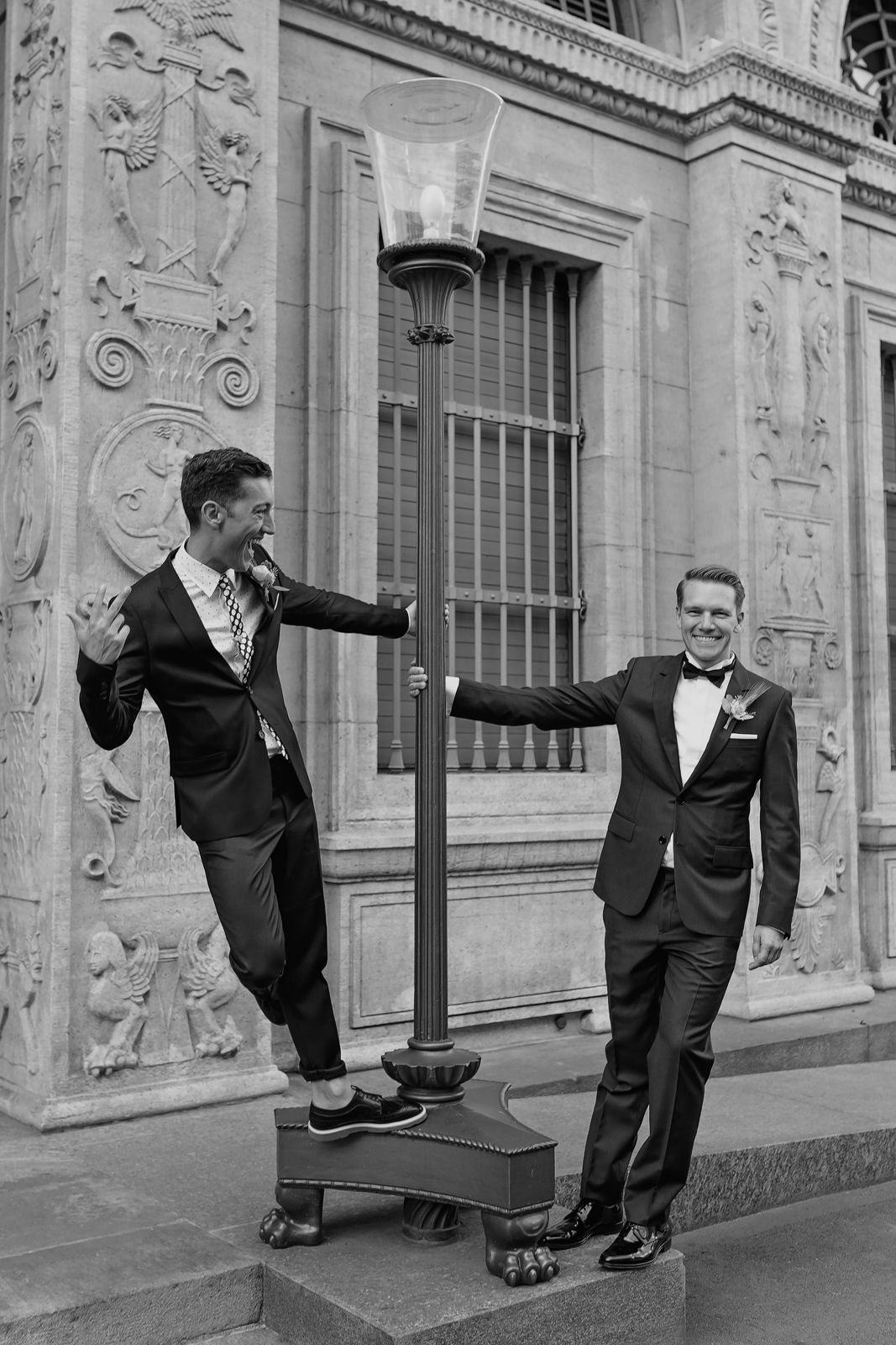 Black and white artistic shot of two grooms posing by a tall, ornate window at a grand Zurich venue.