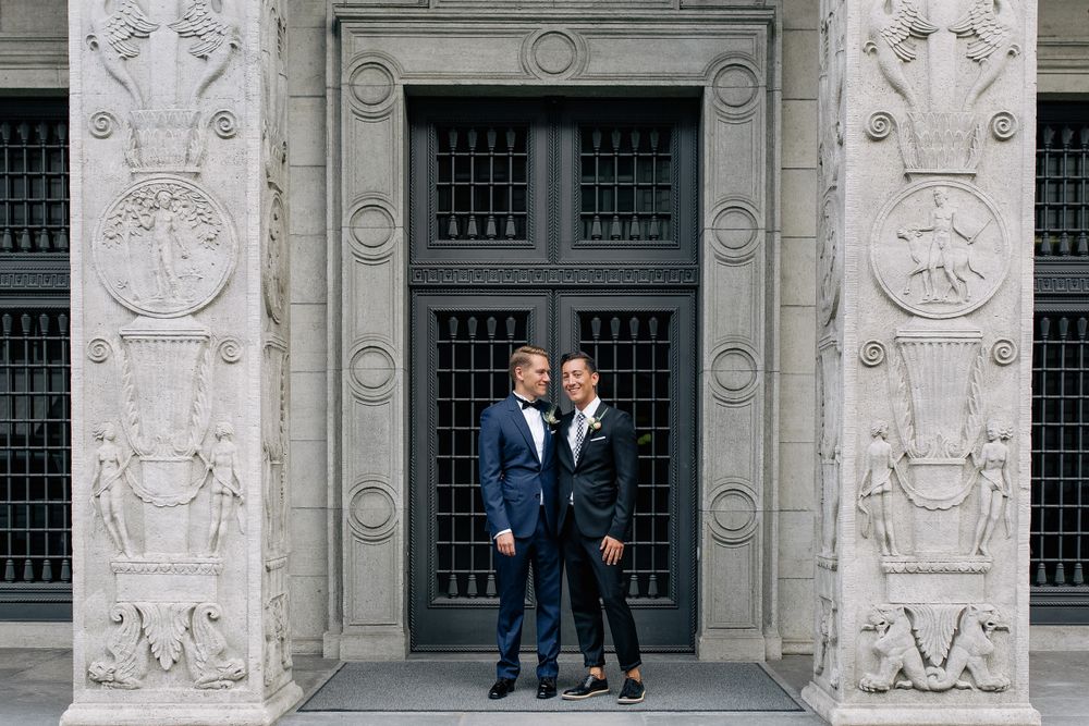 A couple in matching blue suits standing before a large, symmetrical stone doorway at a historic Zurich venue.