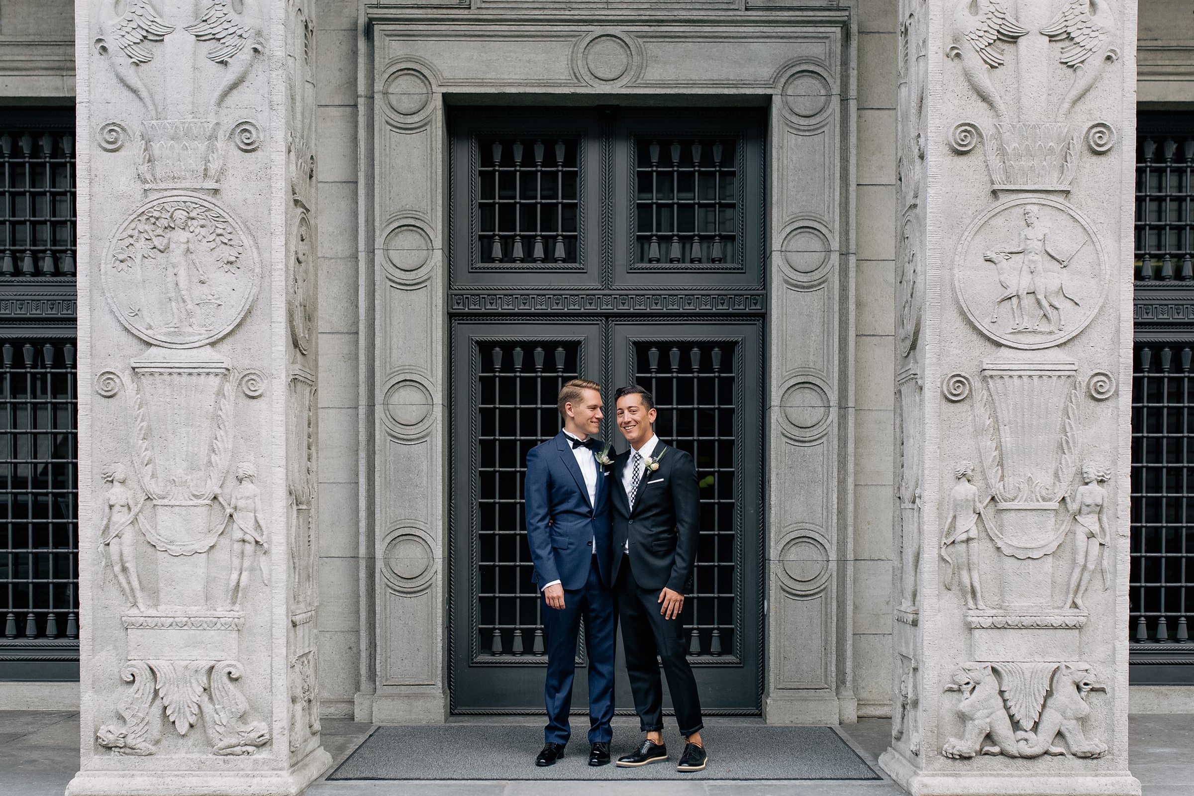 A couple in matching blue suits standing before a large, symmetrical stone doorway at a historic Zurich venue.