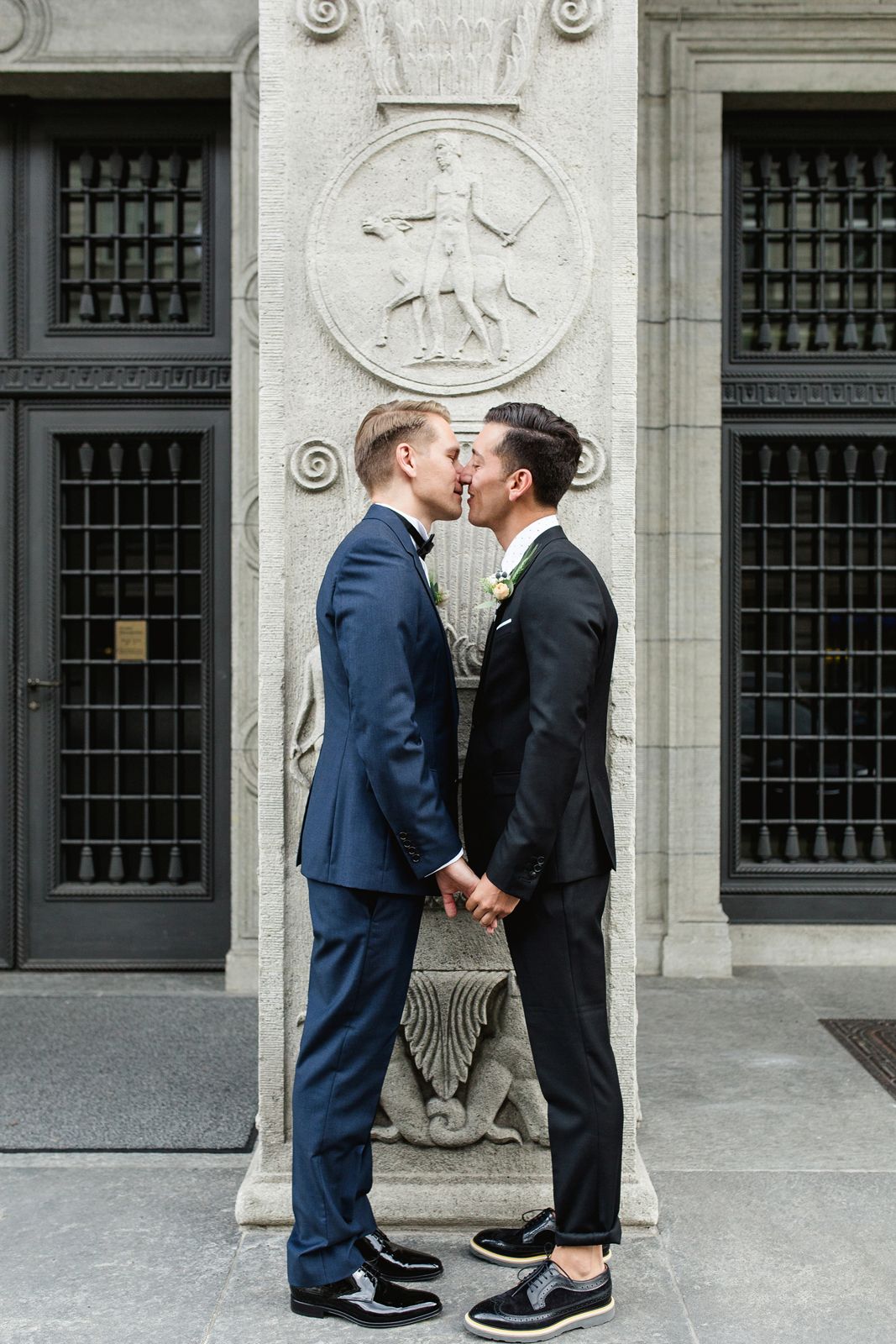 Full-length vertical shot of a couple sharing a romantic kiss in front of a tall, historic black door.