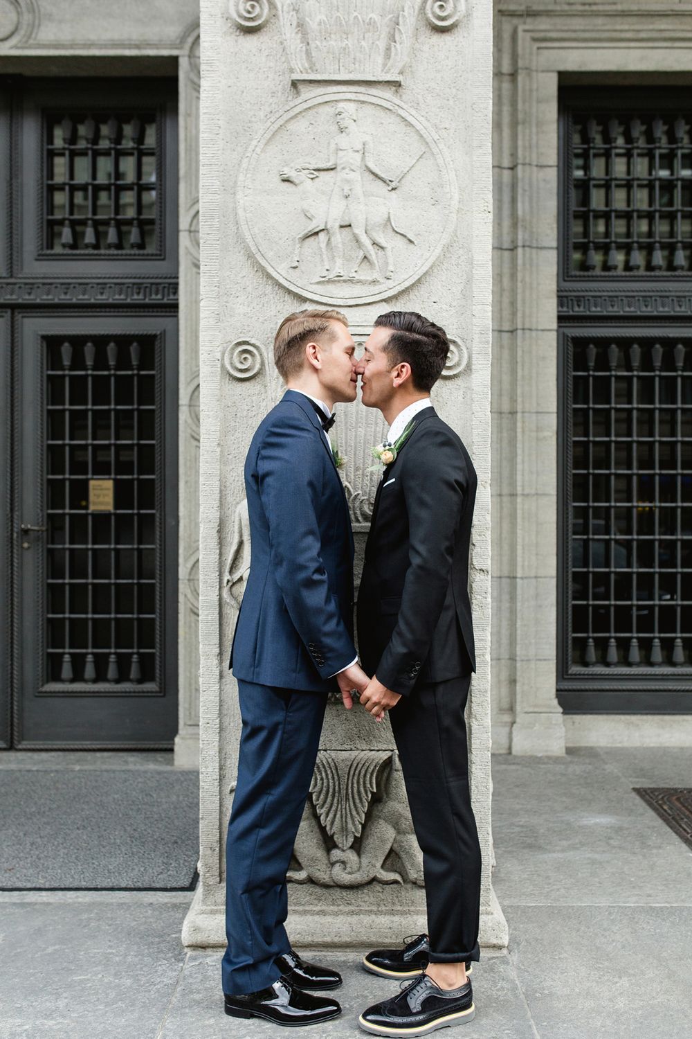 Full-length vertical shot of a couple sharing a romantic kiss in front of a tall, historic black door.