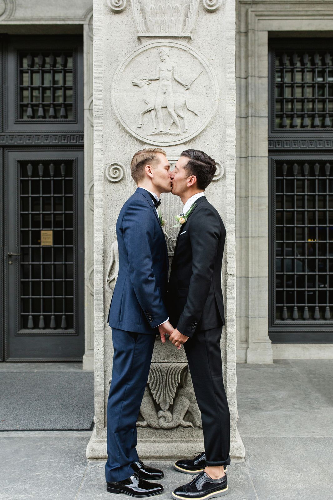 Full-length vertical shot of a couple sharing a romantic kiss in front of a tall, historic black door.