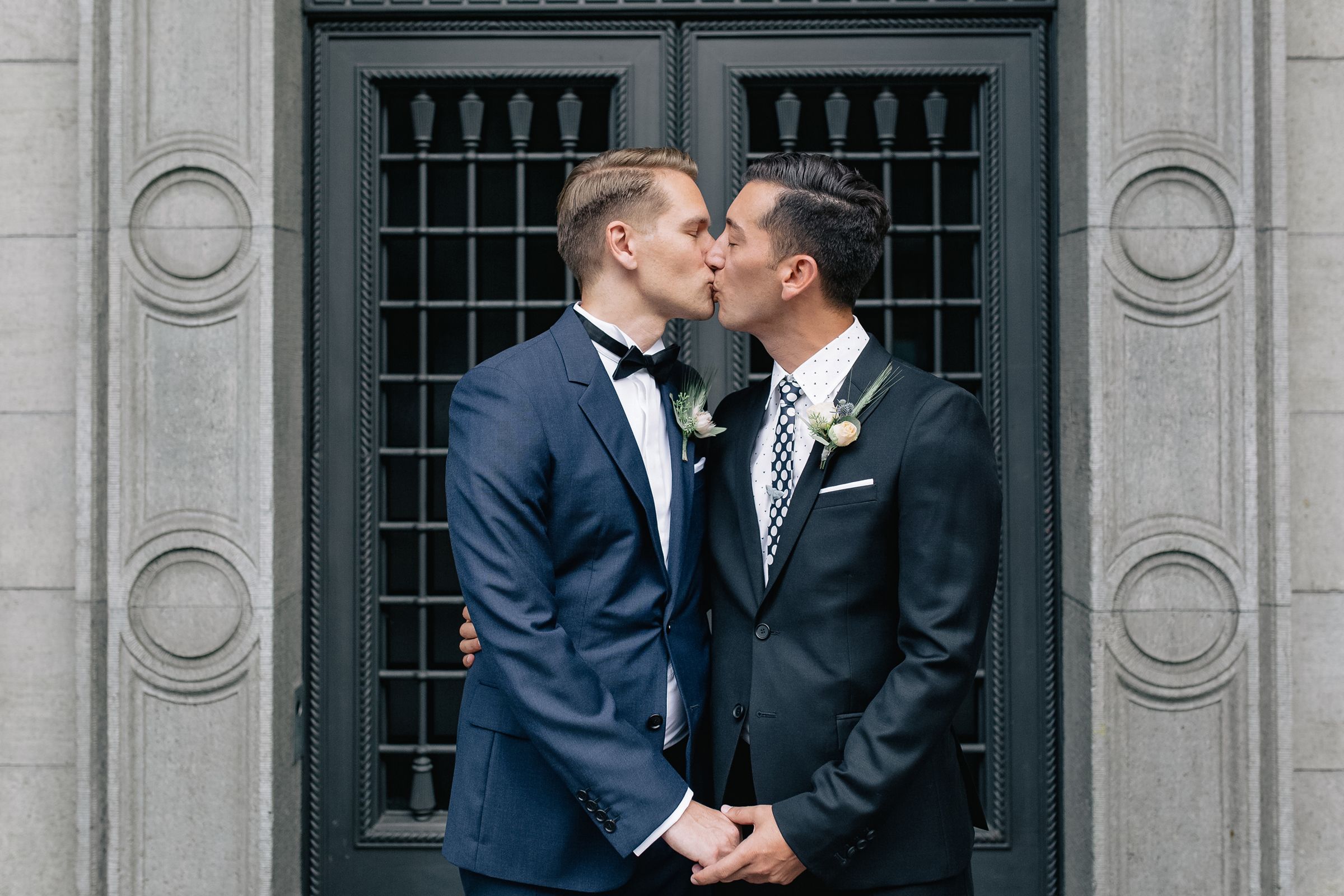 Close-up of a groom kissing his partner's lips in front of a lattice door.