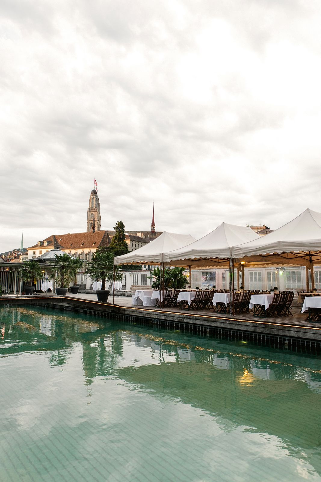 Vertical view of a wedding reception tent by a canal in Zurich with historic buildings in the background.