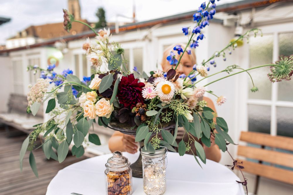 Close-up of a rustic wedding floral centerpiece featuring deep red and blue wildflowers on a white-clothed table.