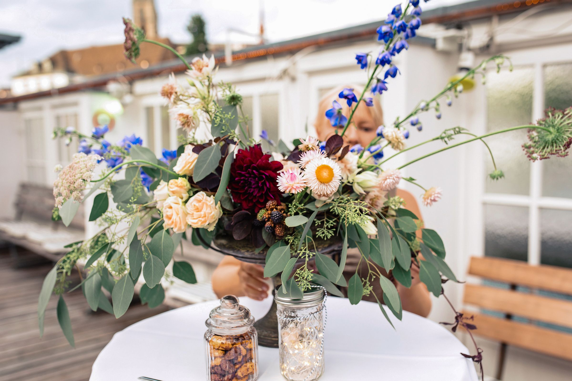 Close-up of a rustic wedding floral centerpiece featuring deep red and blue wildflowers on a white-clothed table.