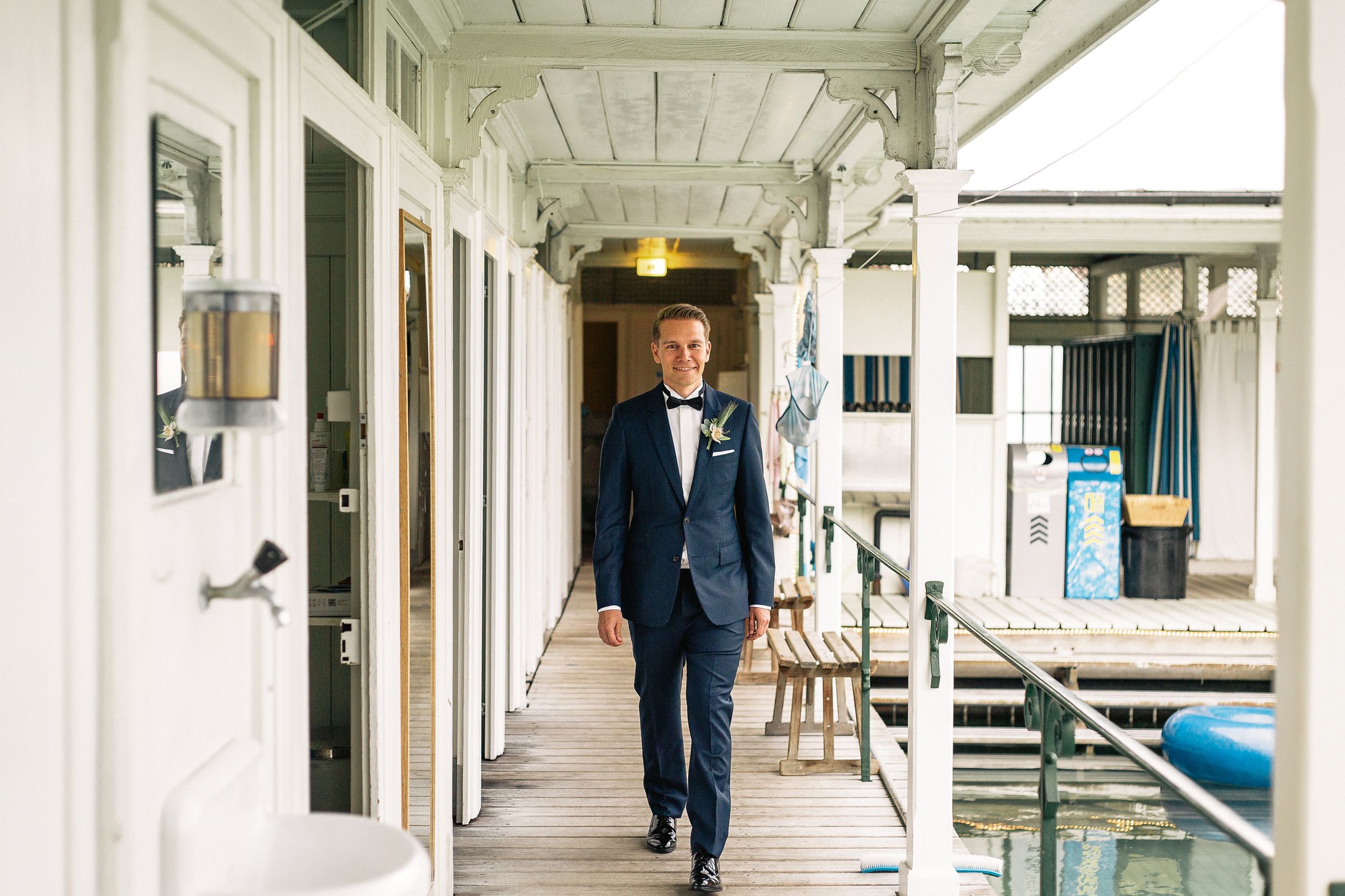 Groom in a dark blue suit walking down a white-pillared hallway at a wedding venue in Zurich.