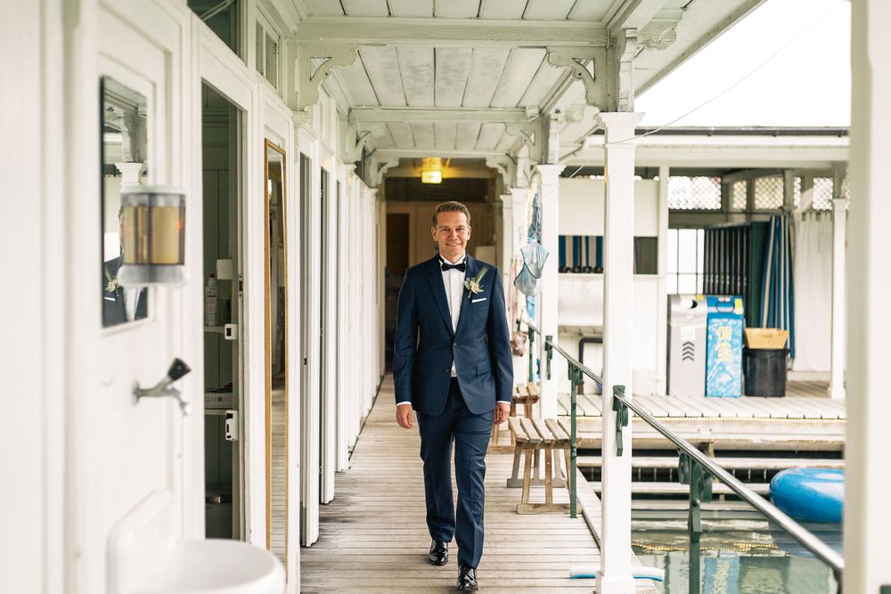 Groom in a dark blue suit walking down a white-pillared hallway at a wedding venue in Zurich.