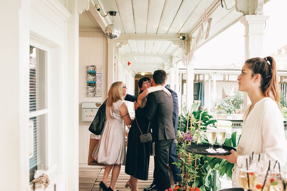 A group of wedding guests mingling and talking on a bright, airy outdoor patio area.