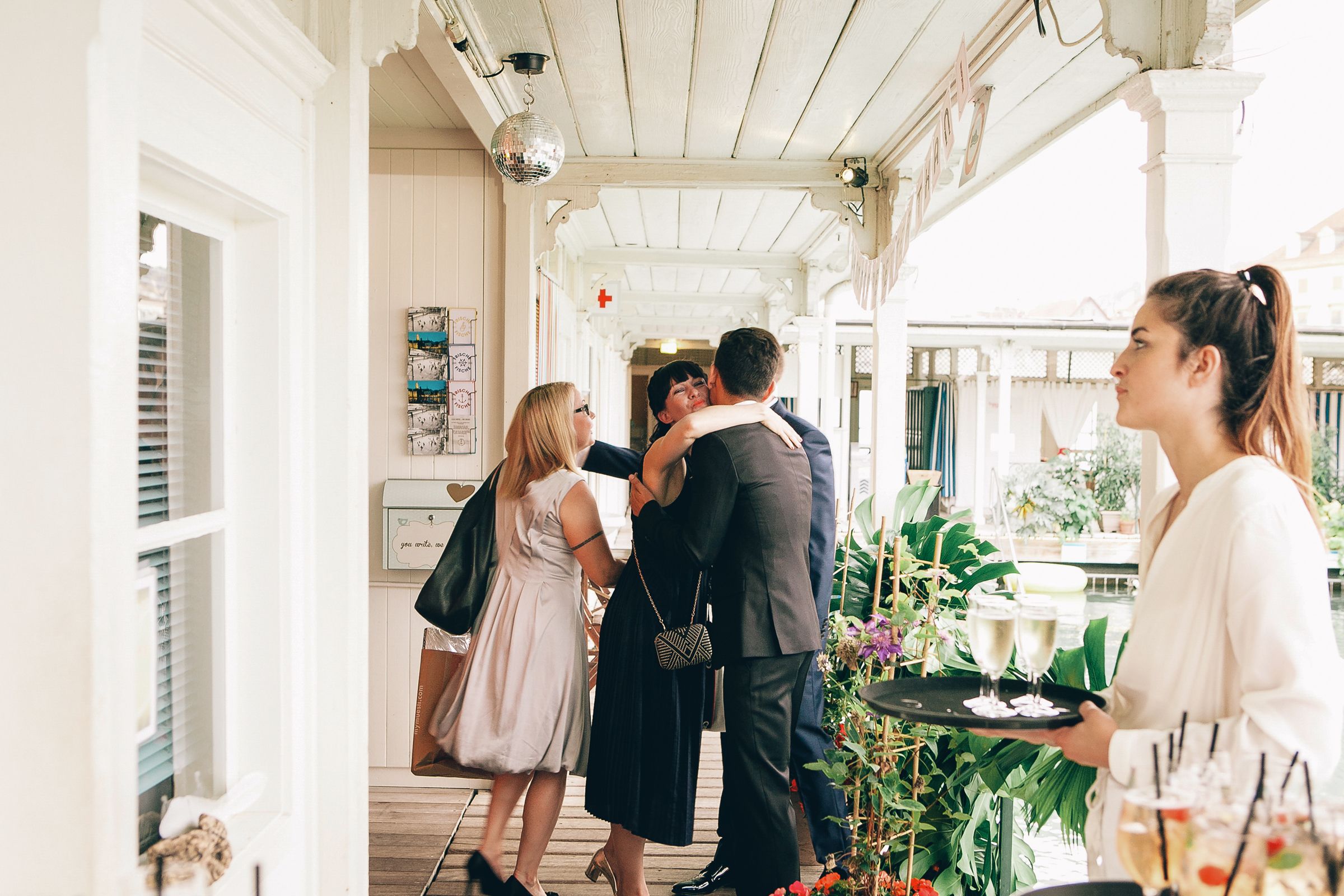 A group of wedding guests mingling and talking on a bright, airy outdoor patio area.