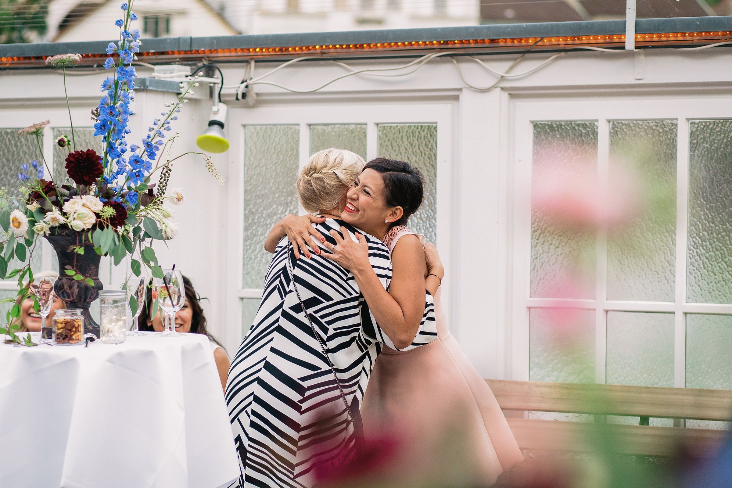 Emotional candid of two wedding guests sharing a heartfelt hug at an outdoor reception in Zurich.