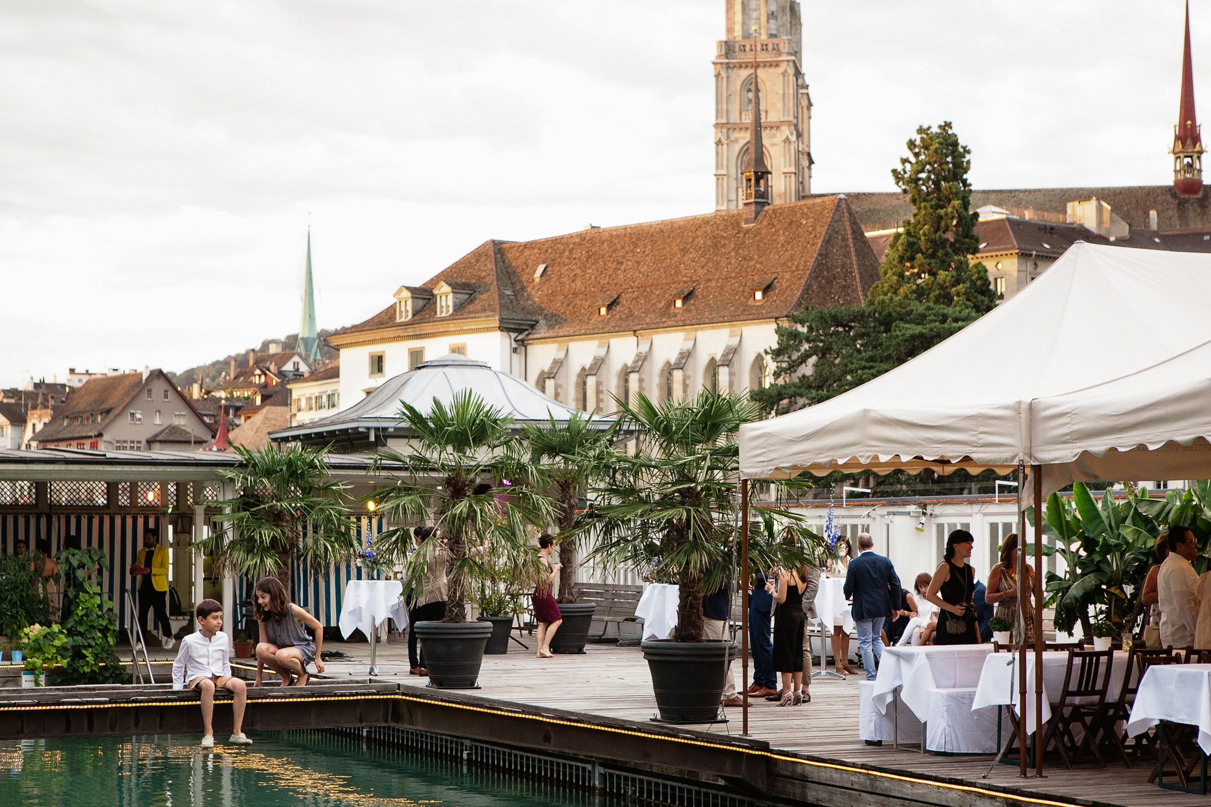 Individuals gather at tables in a picturesque courtyard, surrounded by lush greenery and a calming pool.