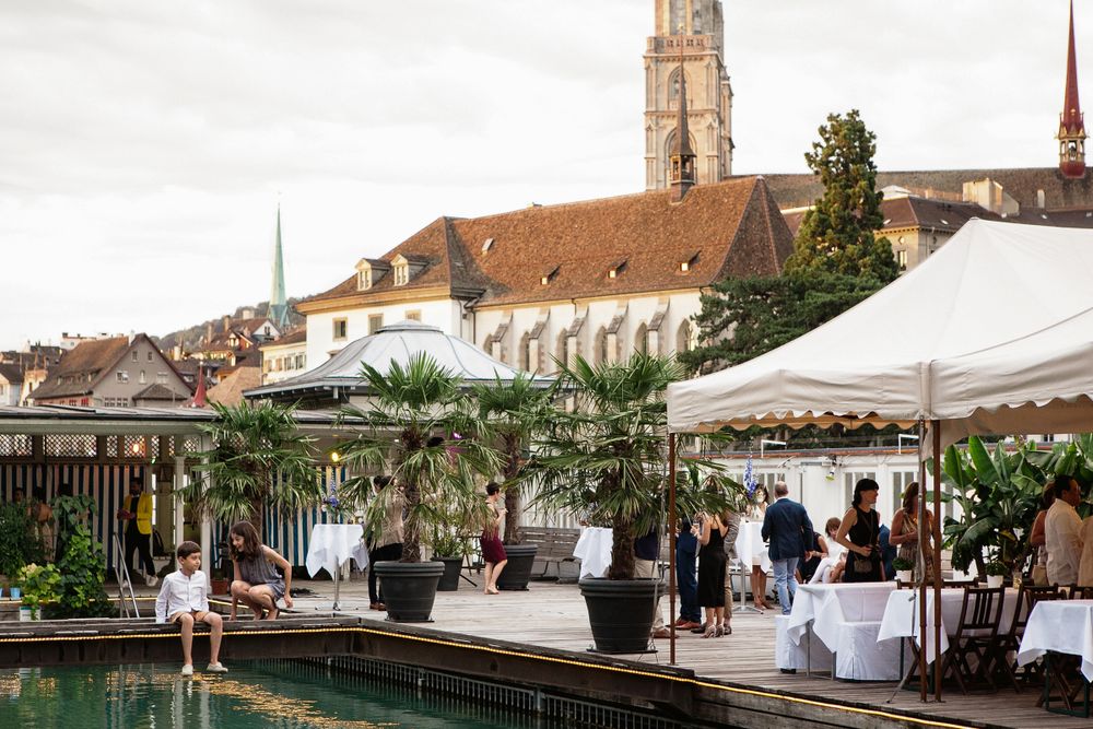 Individuals gather at tables in a picturesque courtyard, surrounded by lush greenery and a calming pool.