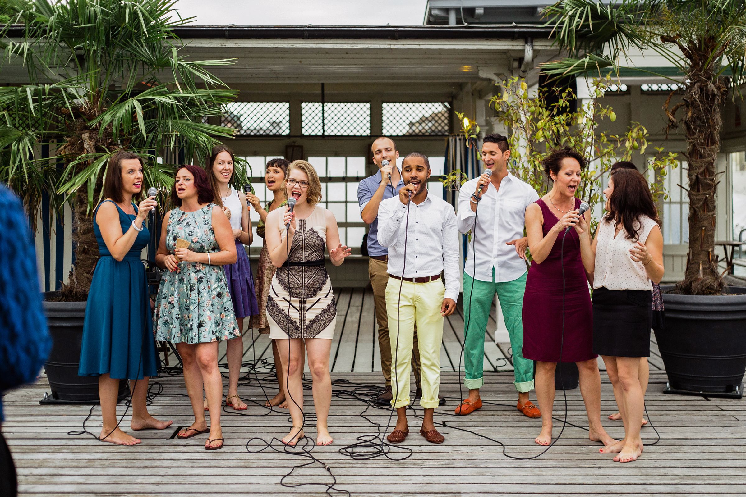 Several people on a deck, microphones in hand, singing.