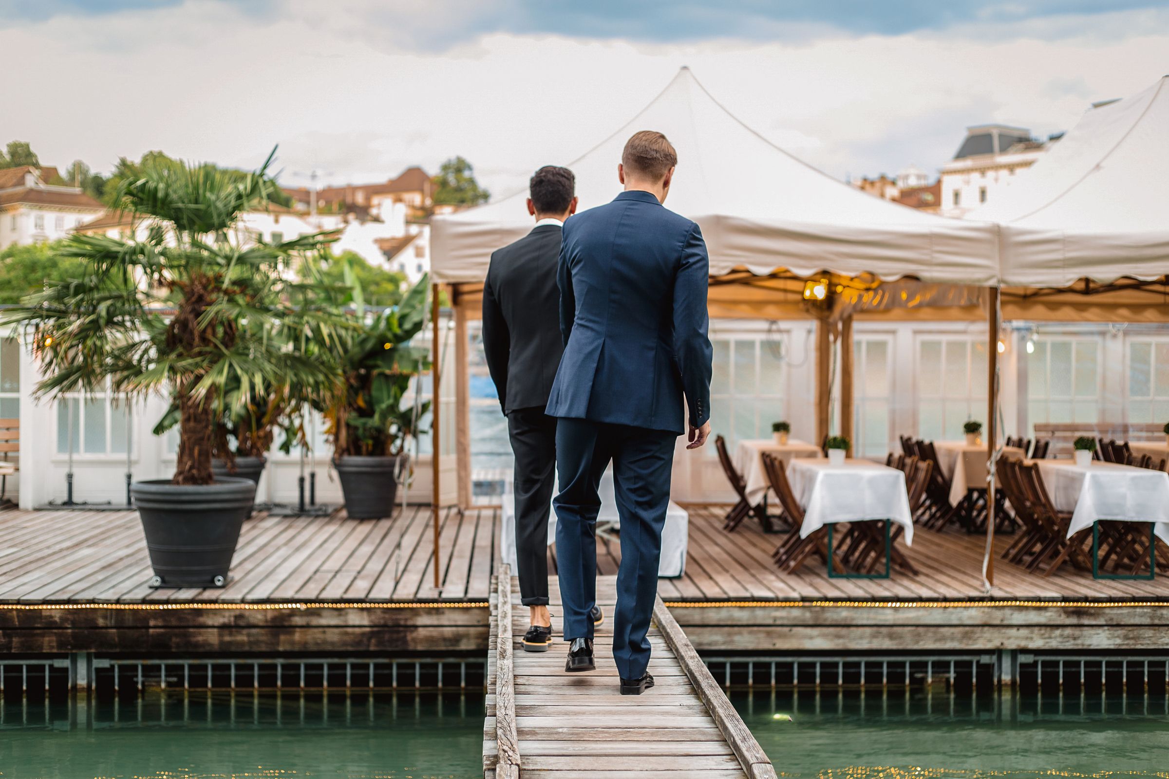 Two men in suits walking along a dock, surrounded by water.