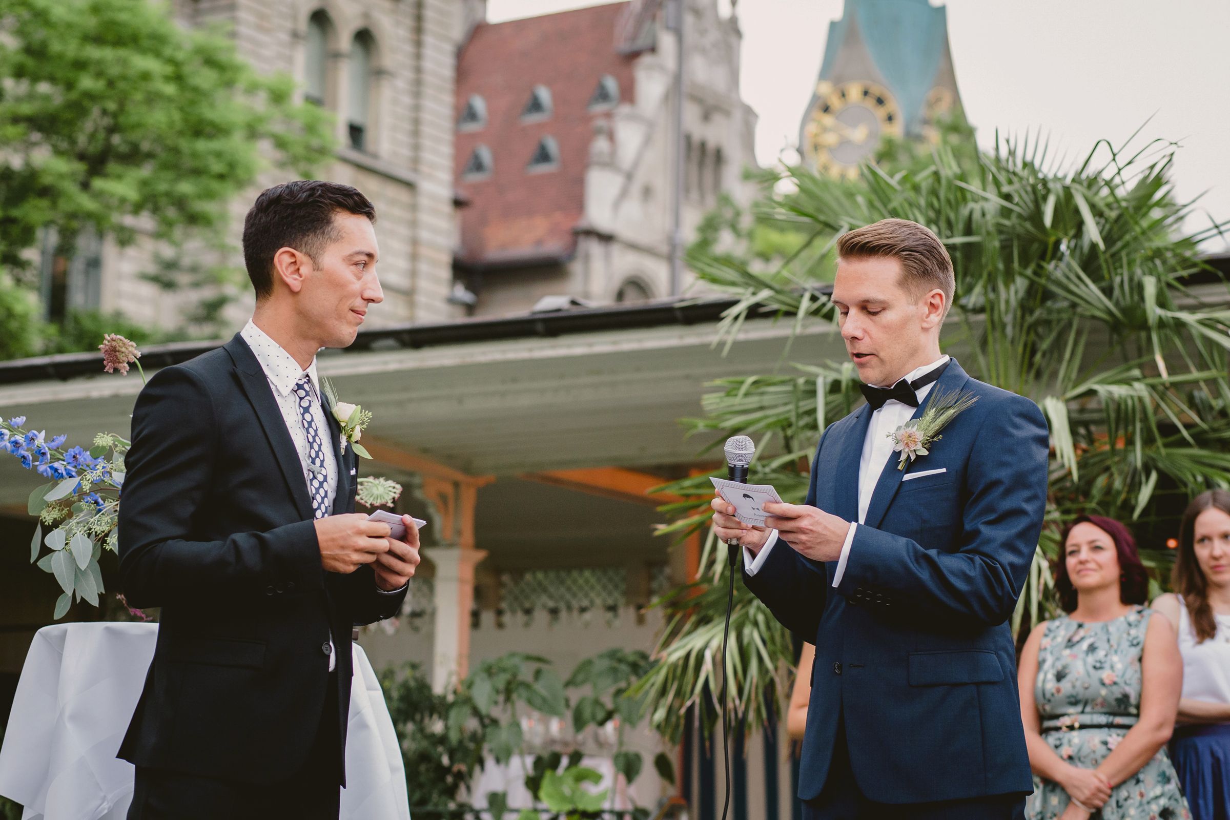 An elegant wedding ceremony in Zurich, showcasing a gay couple exchanging vows amidst a scenic backdrop and joyful attendees.