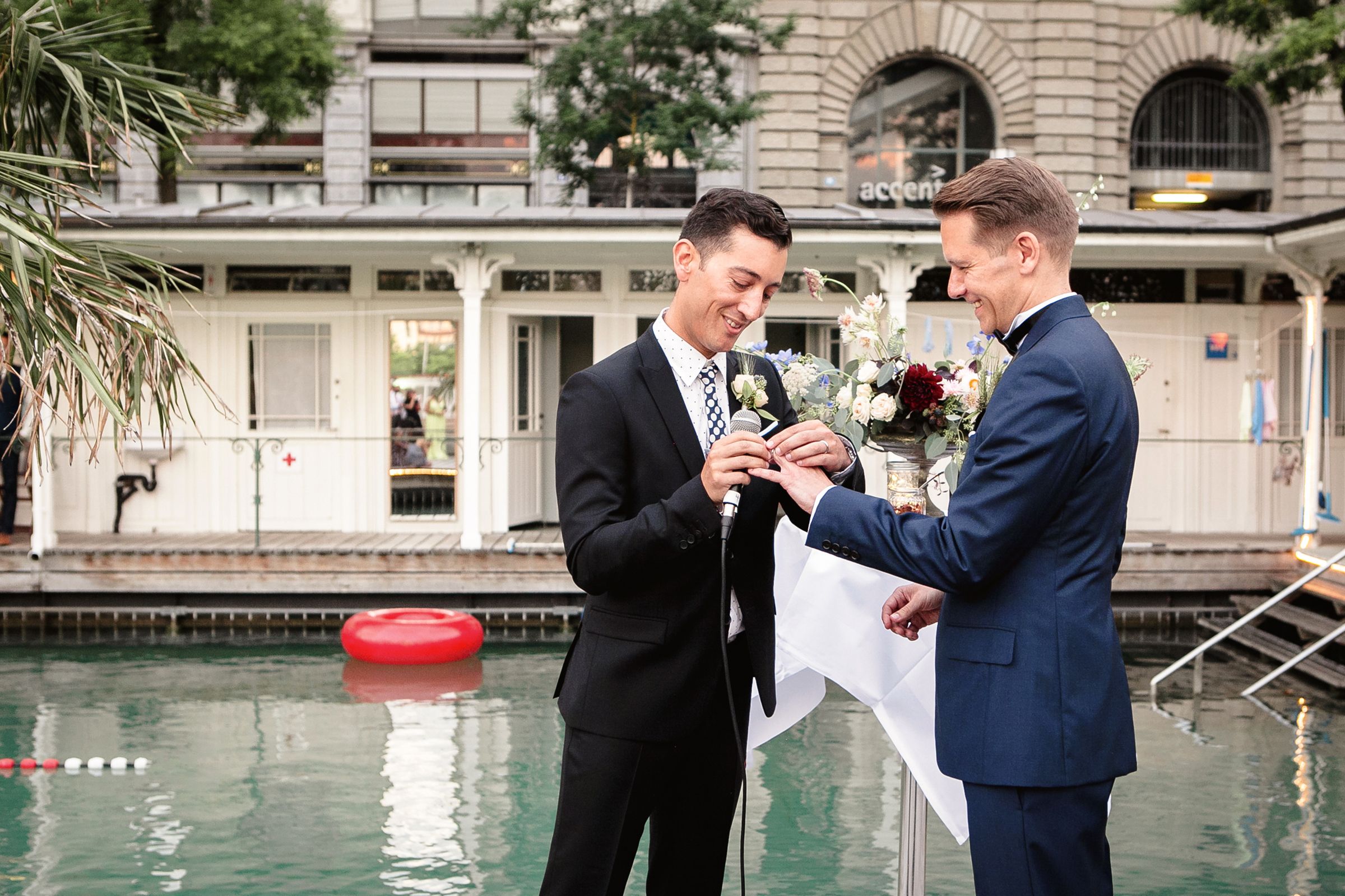 A gay couple exchanging rings next to a pool at wedding