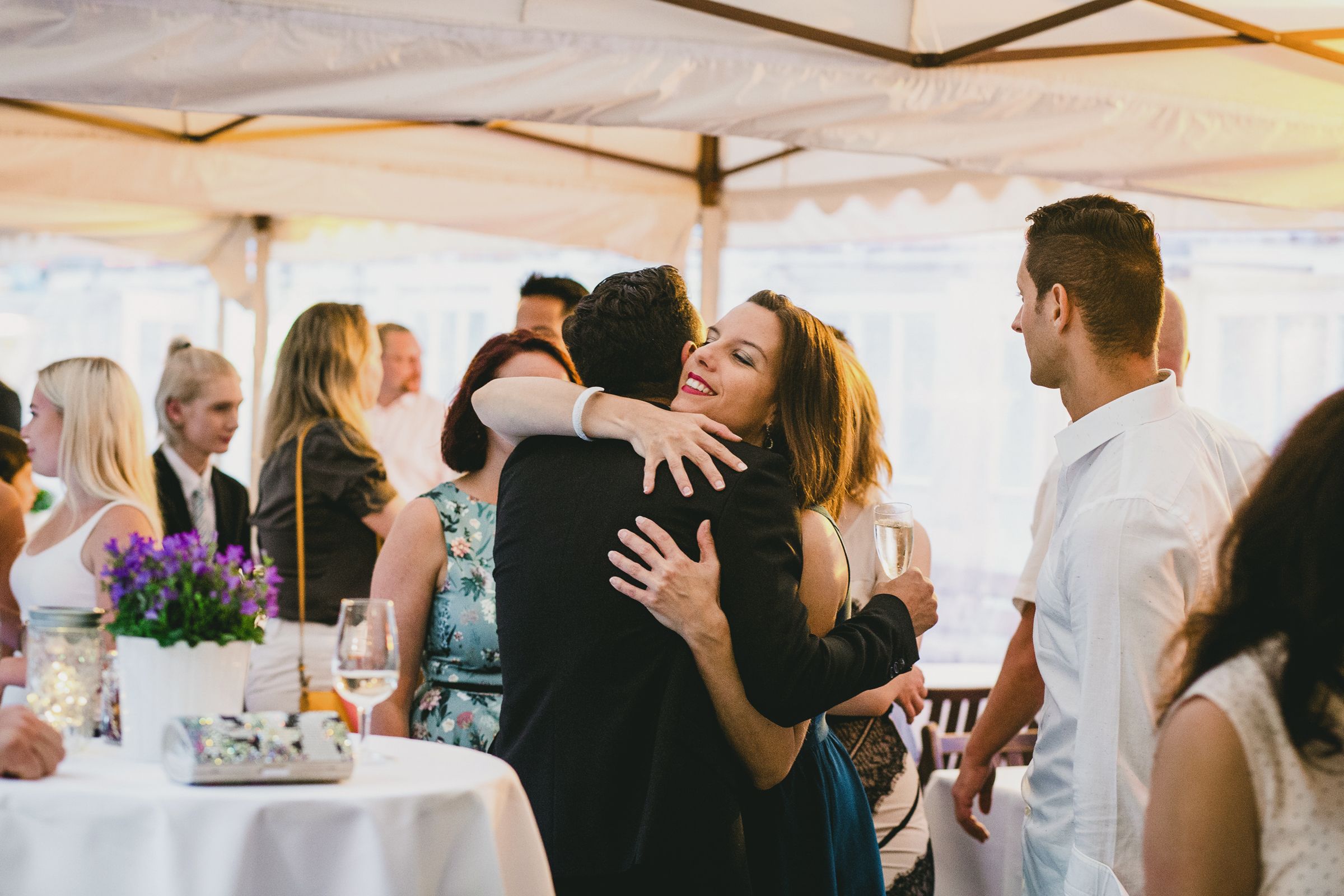 A brunette woman hugging a man, looking happy, at a party.