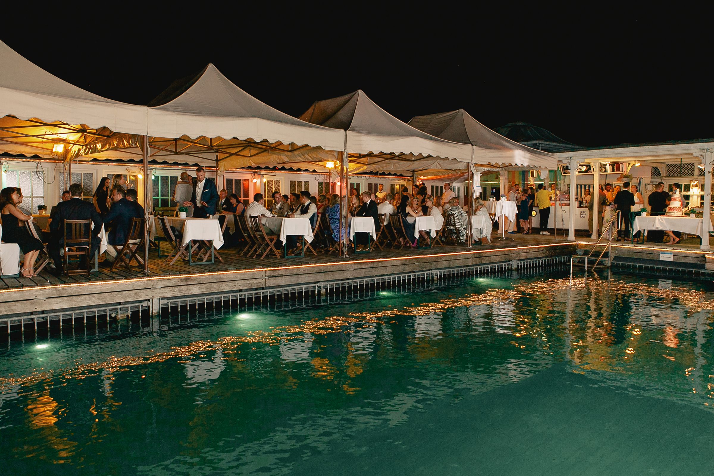Nighttime view of an illuminated wedding reception tent reflected in a swimming pool in Zurich.