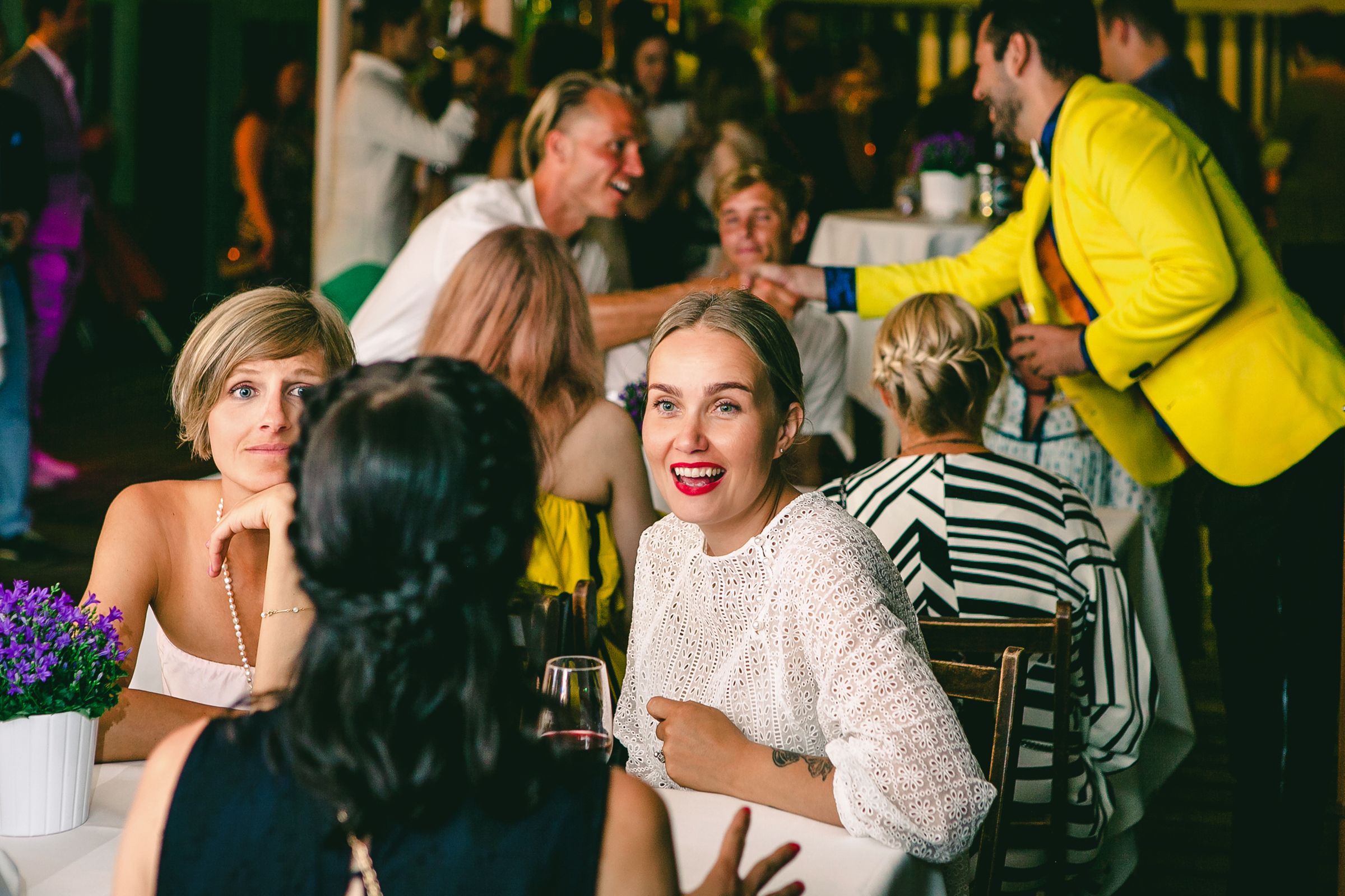 Candid shot of wedding guests laughing and talking around a dinner table during a reception.