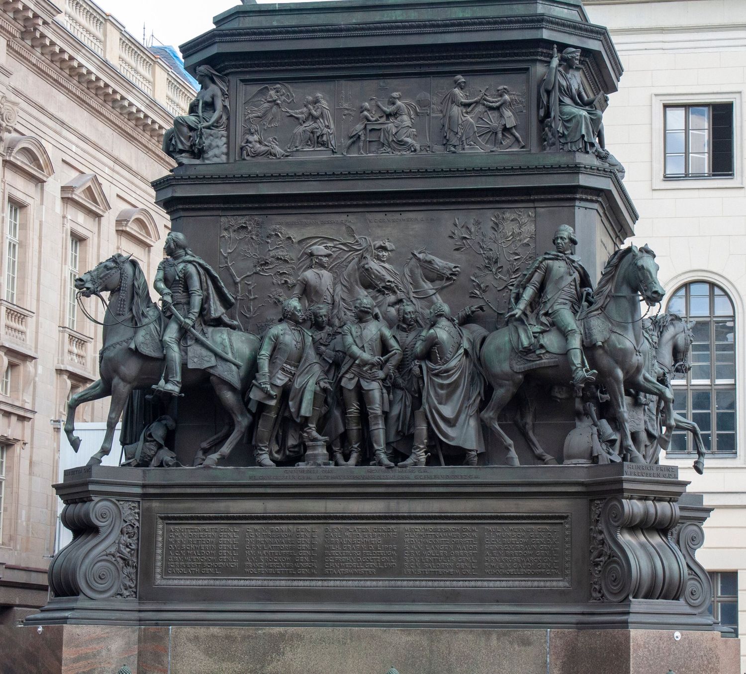 A dark bronze sculptural relief depicting historical figures and horses on an ornate monument base in a classical style.