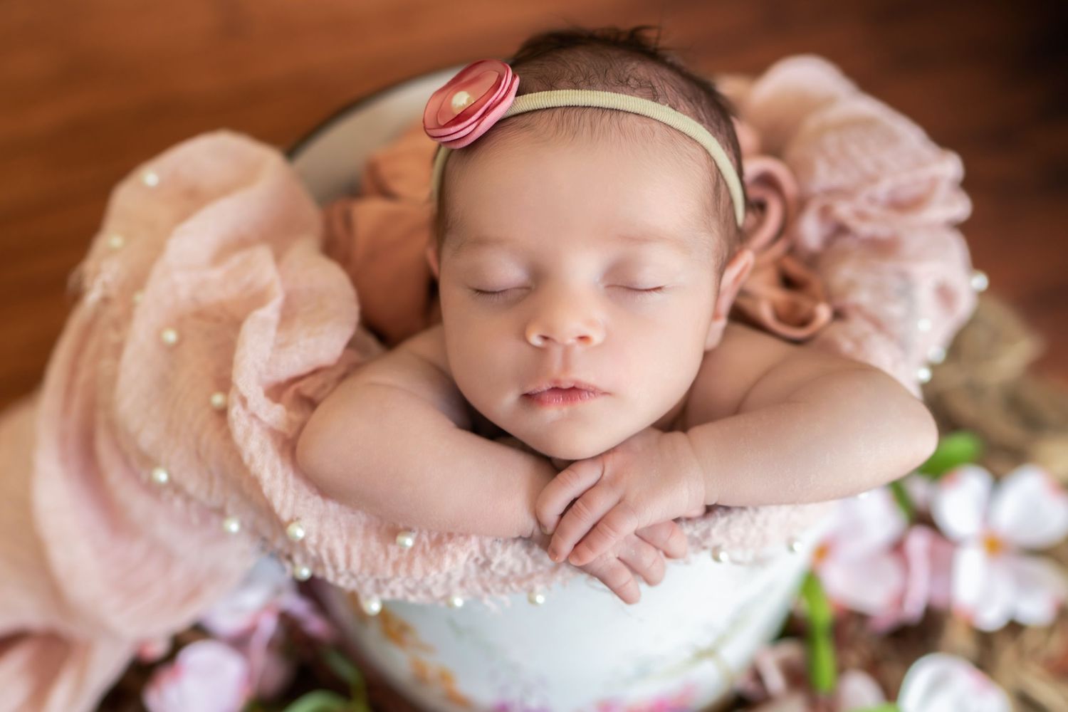 Sleeping newborn with pink bow headband surrounded by soft pink tones.
