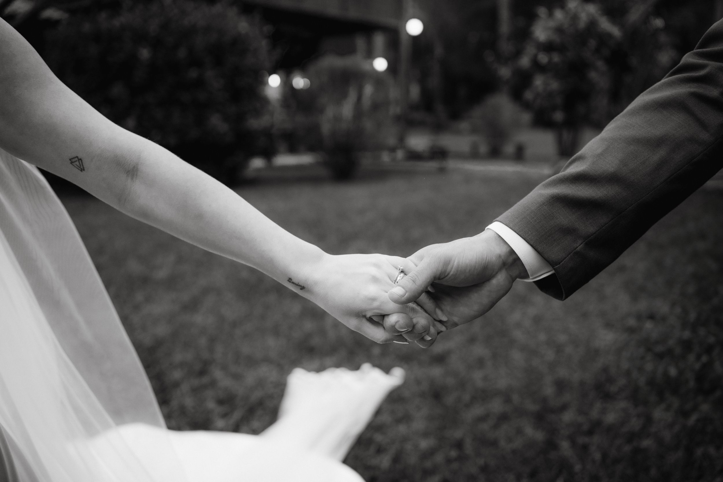 Close-up of newlyweds holding hands in a garden setting, captured in black and white.
