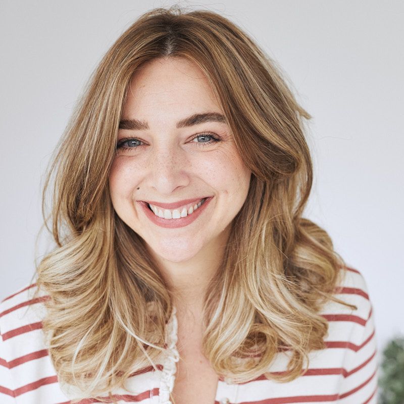 Portrait against white background wearing red and white striped top with wavy blonde hair.