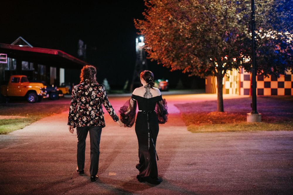 Couple walking hand in hand at night past colorful trees and vintage cars.