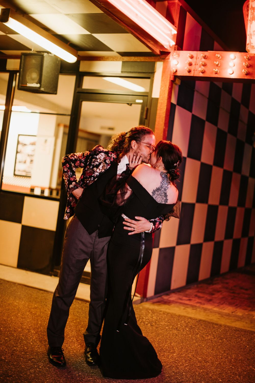 Couple sharing a passionate kiss outside a retro diner with checkered decor at night.