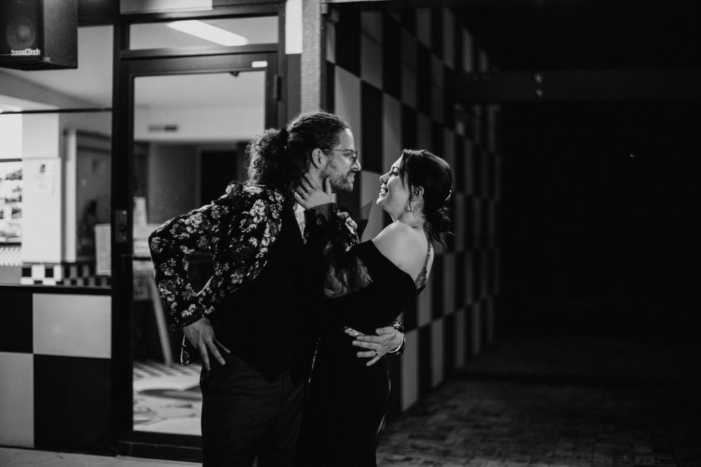 Black and white photo of couple sharing a tender kiss near a checkered wall.