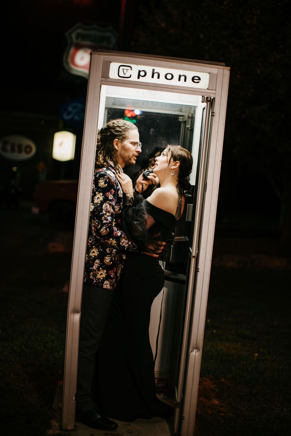Romantic couple sharing an intimate moment inside a vintage phone booth at night.