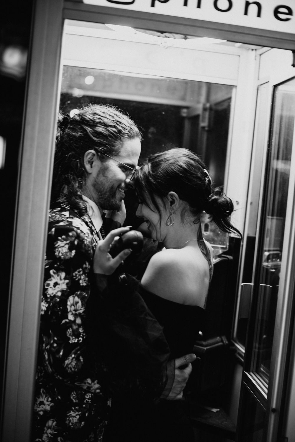 Black and white photo of couple laughing together inside a vintage phone booth.