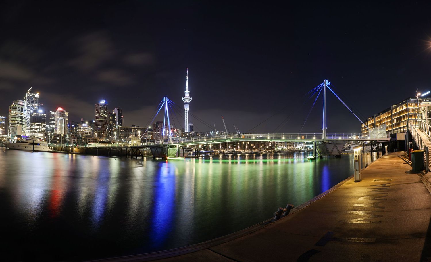 Auckland's waterfront sparkles under city lights, with the Sky Tower and bridge lit in brilliant colour.